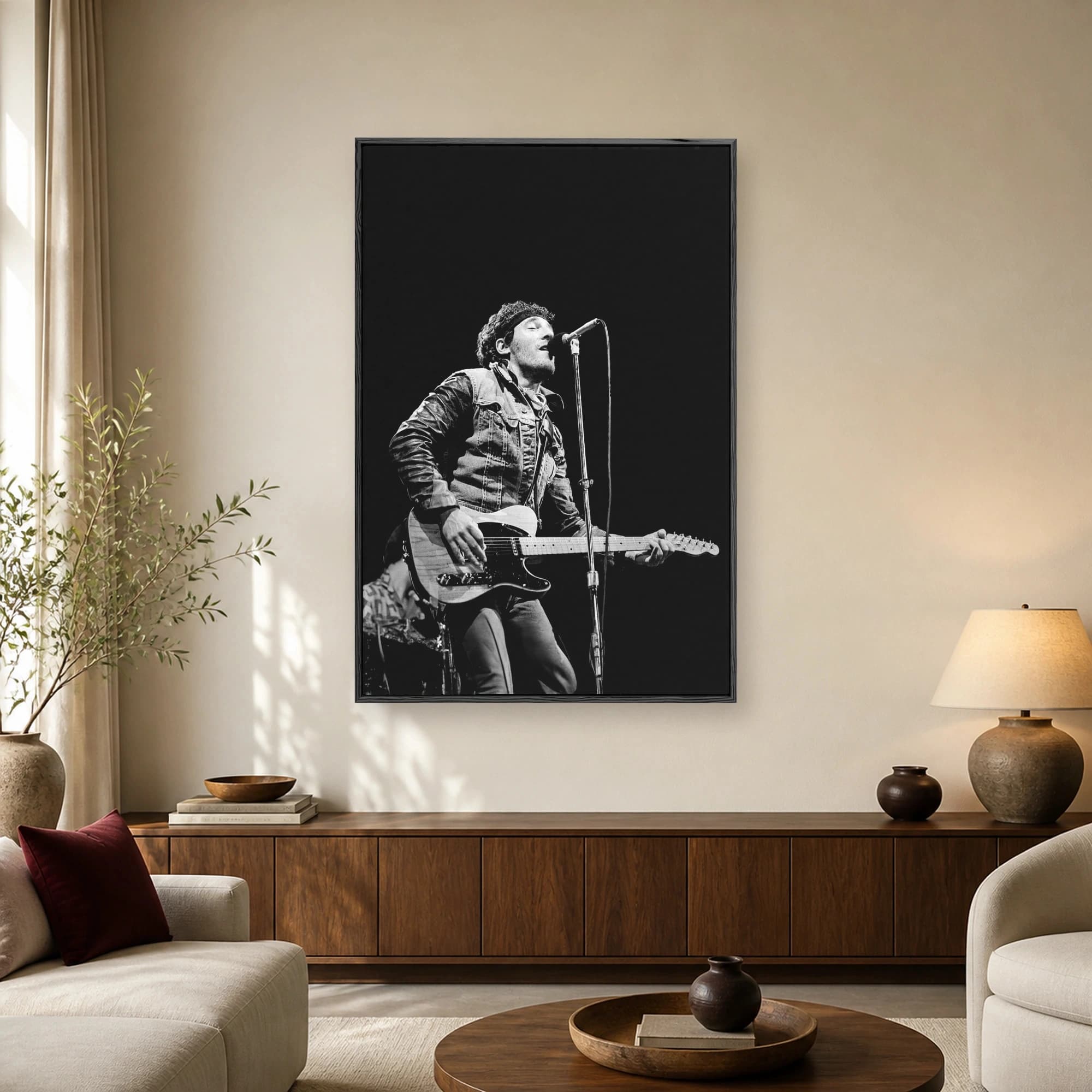 Black and white concert photograph of Bruce Springsteen singing into a microphone while playing an electric guitar against a dark background.
