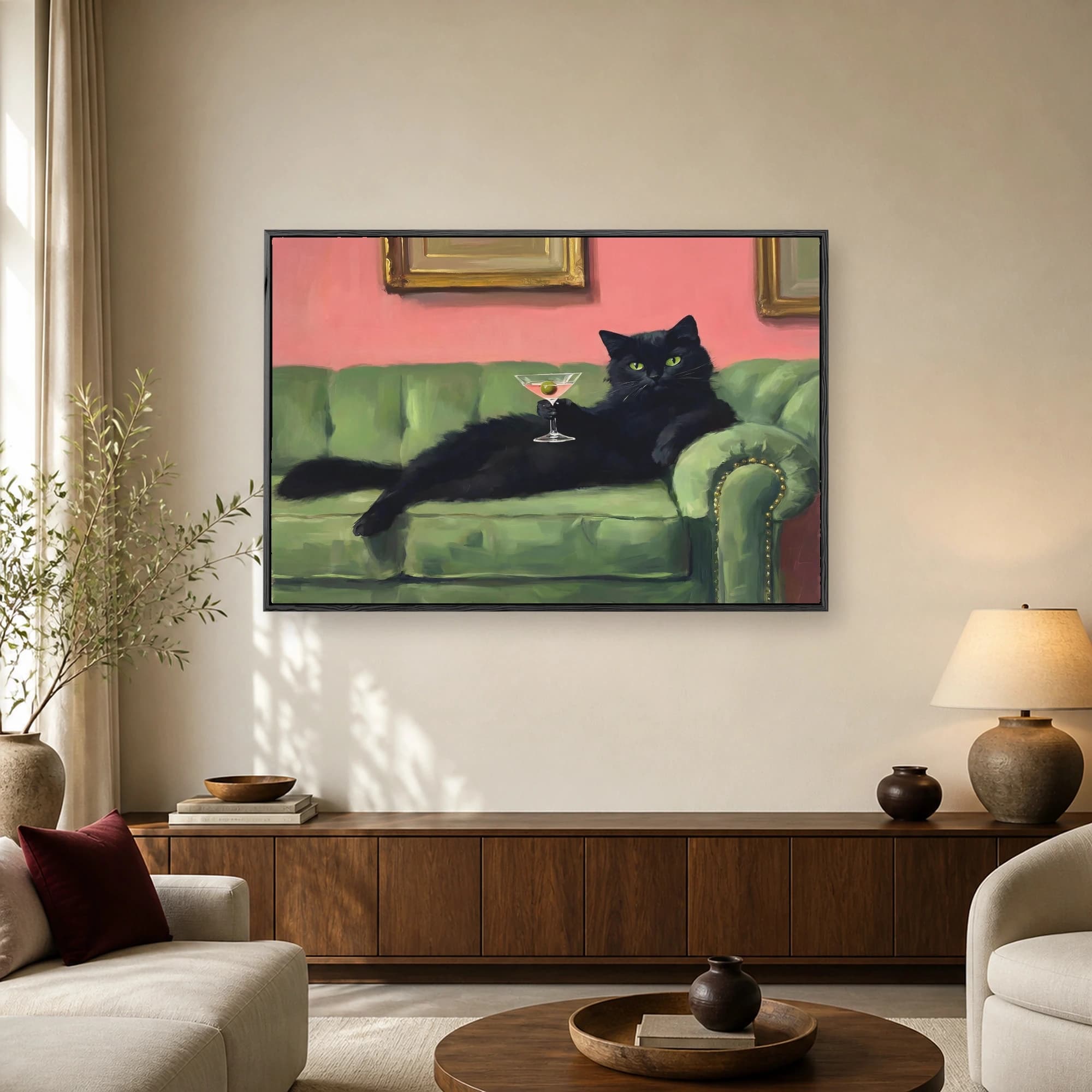 A sleek black cat with green eyes lounging on a green sofa and holding a martini glass with an olive against a pink wall.
