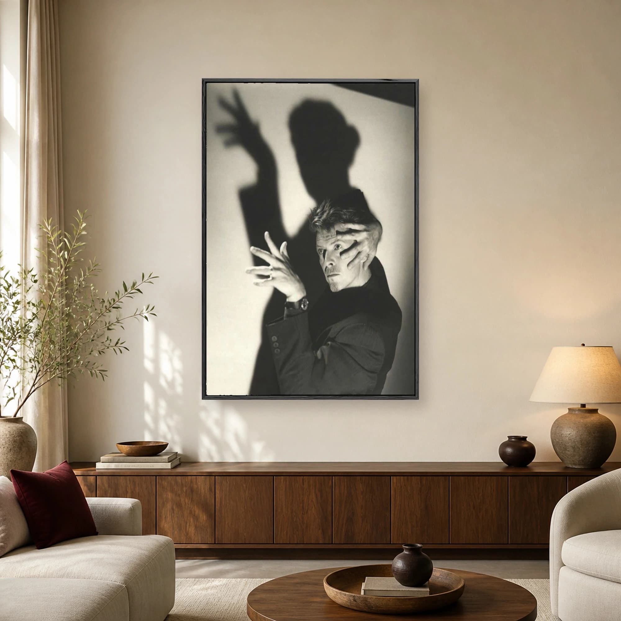Black and white portrait of David Bowie posing with an expressive hand gesture and a dramatic shadow cast on the wall behind him.