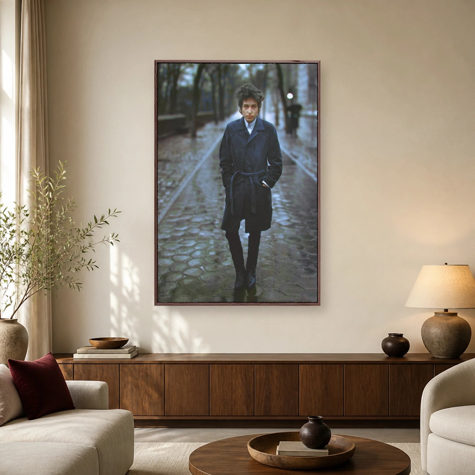 A photographic portrait of Bob Dylan wearing a dark coat and boots while walking on a wet cobblestone path lined with trees.