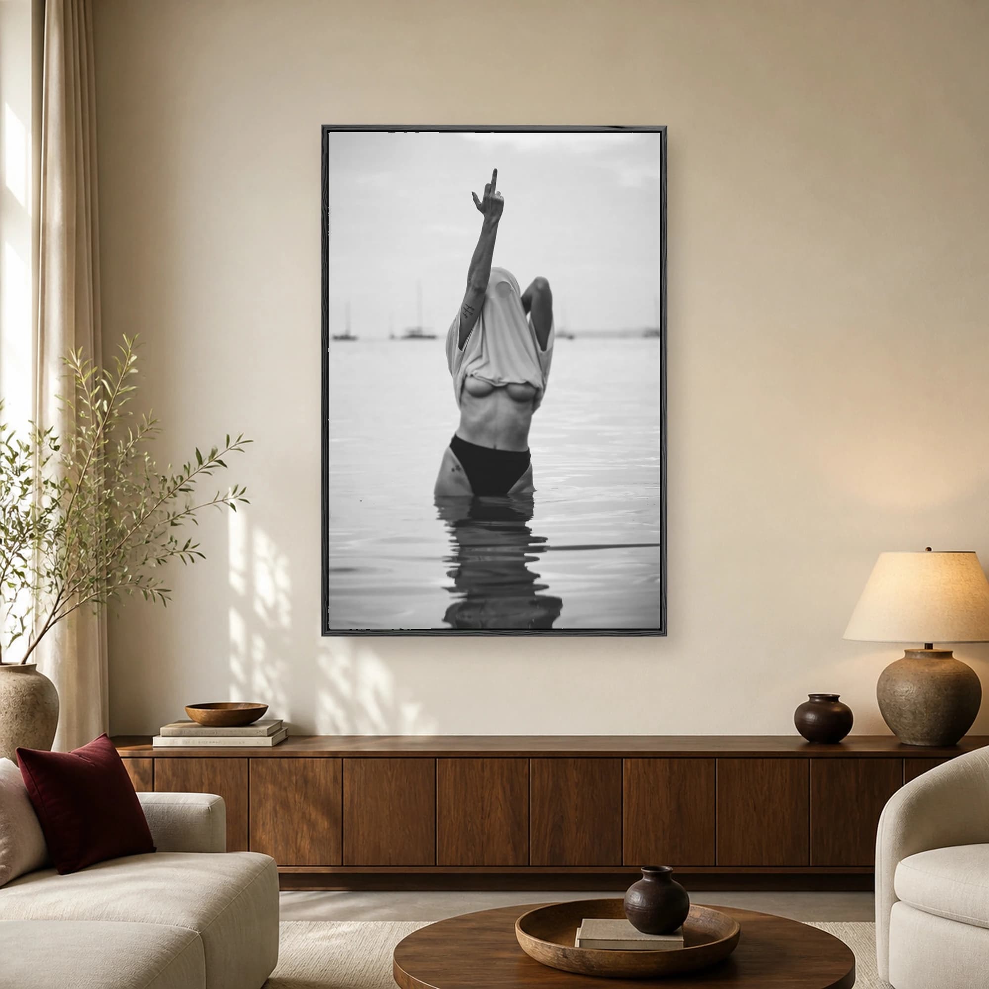 A black and white photograph of a figure waist deep in water with a shirt over their head, holding up a middle finger gesture.
