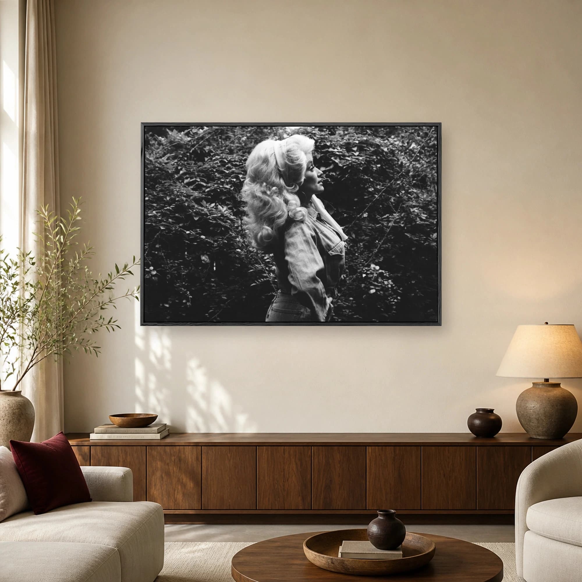 Black and white profile portrait of Dolly Parton with voluminous blonde hair and denim shirt standing in front of lush leaves.
