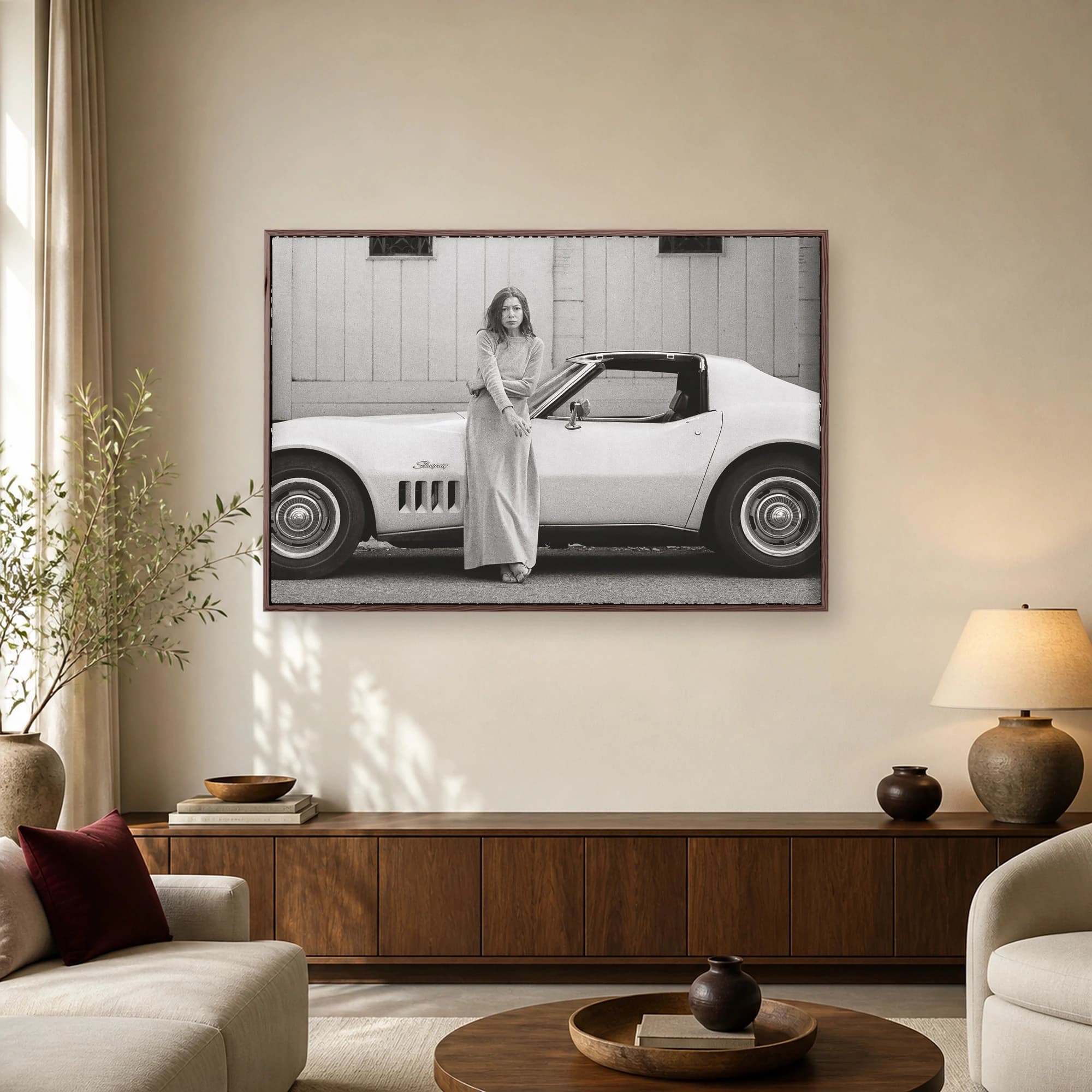 Monochrome photograph of author Joan Didion standing next to a white Corvette Stingray in Los Angeles.