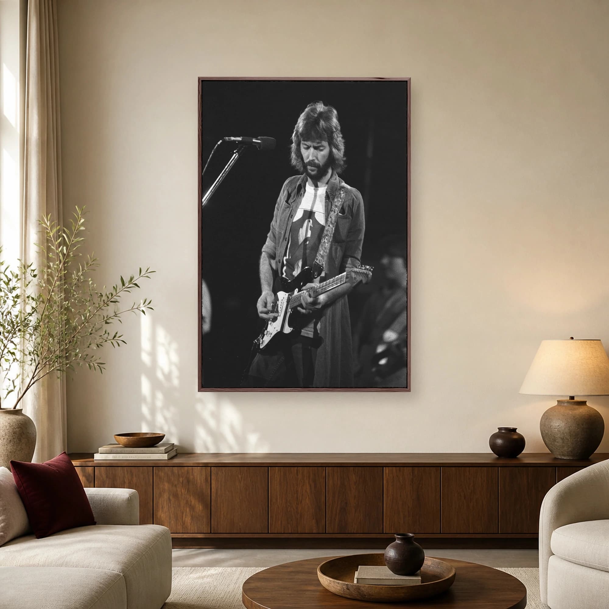 Black and white photograph of Eric Clapton performing live on stage, holding an electric guitar with a vintage microphone nearby.