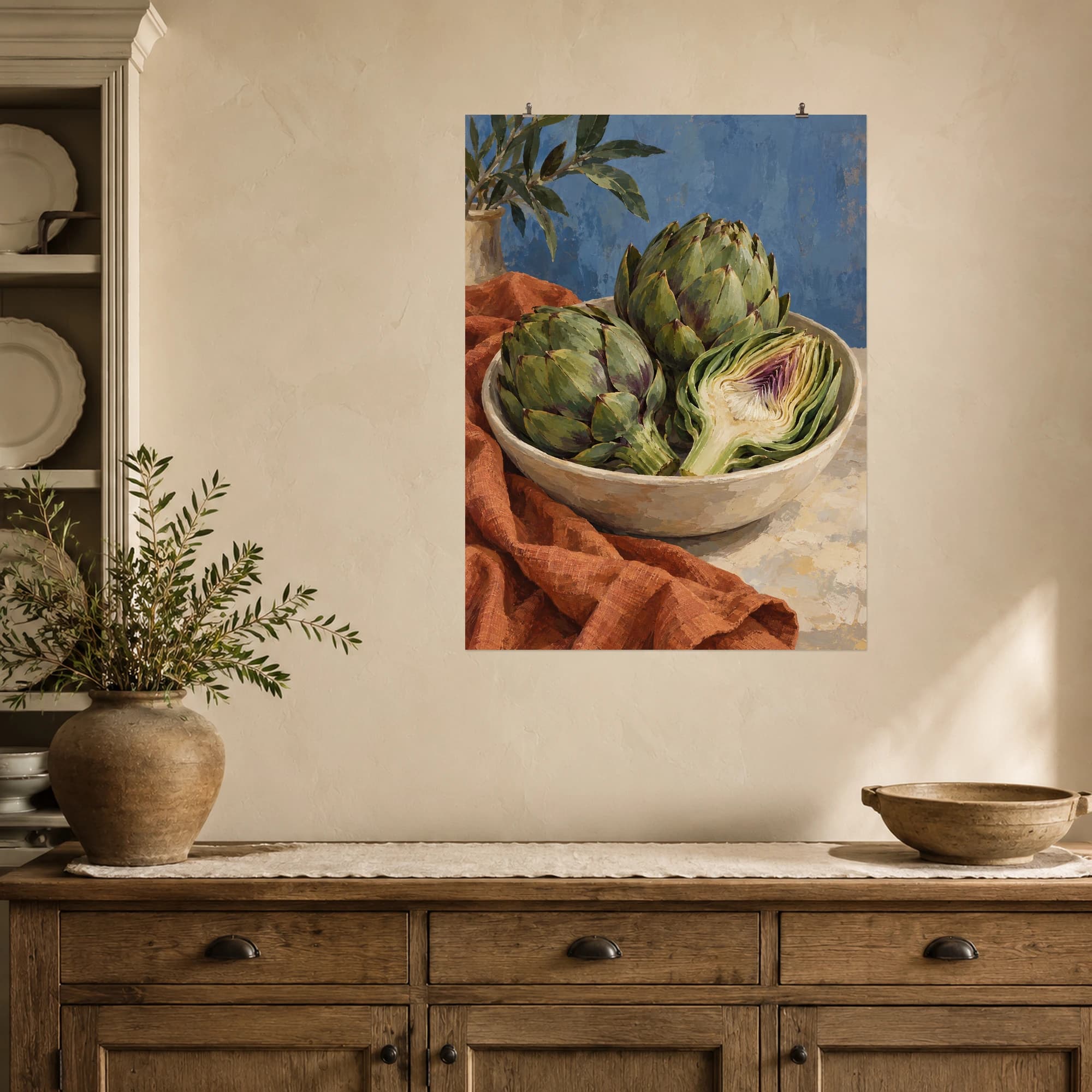 Green artichokes rest in a cream bowl beside rust colored linen. A sliced artichoke reveals its layered center, while dusty blue provides a calm backdrop.