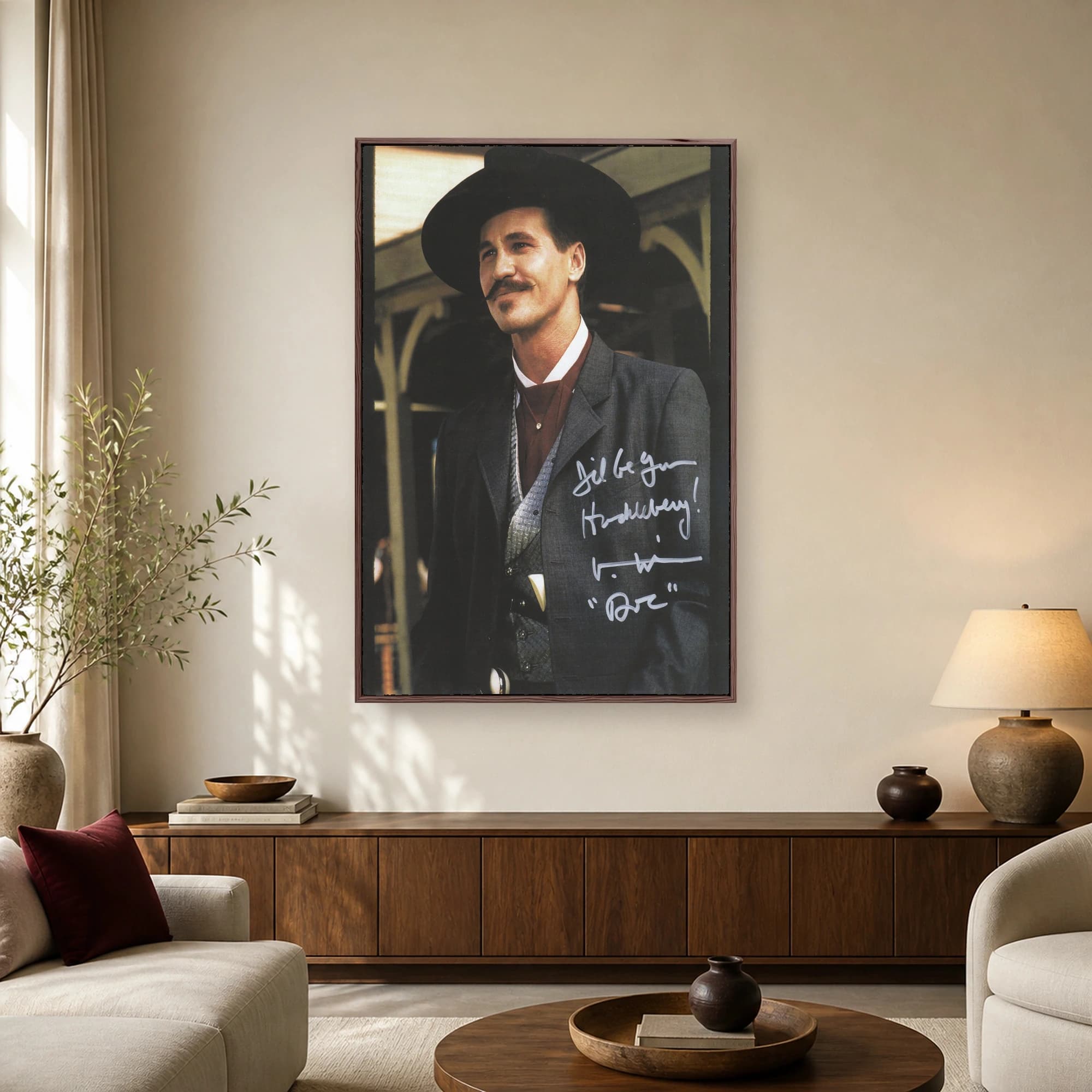 Portrait of Val Kilmer as Doc Holliday wearing a black hat and grey suit, featuring a handwritten quote overlay.