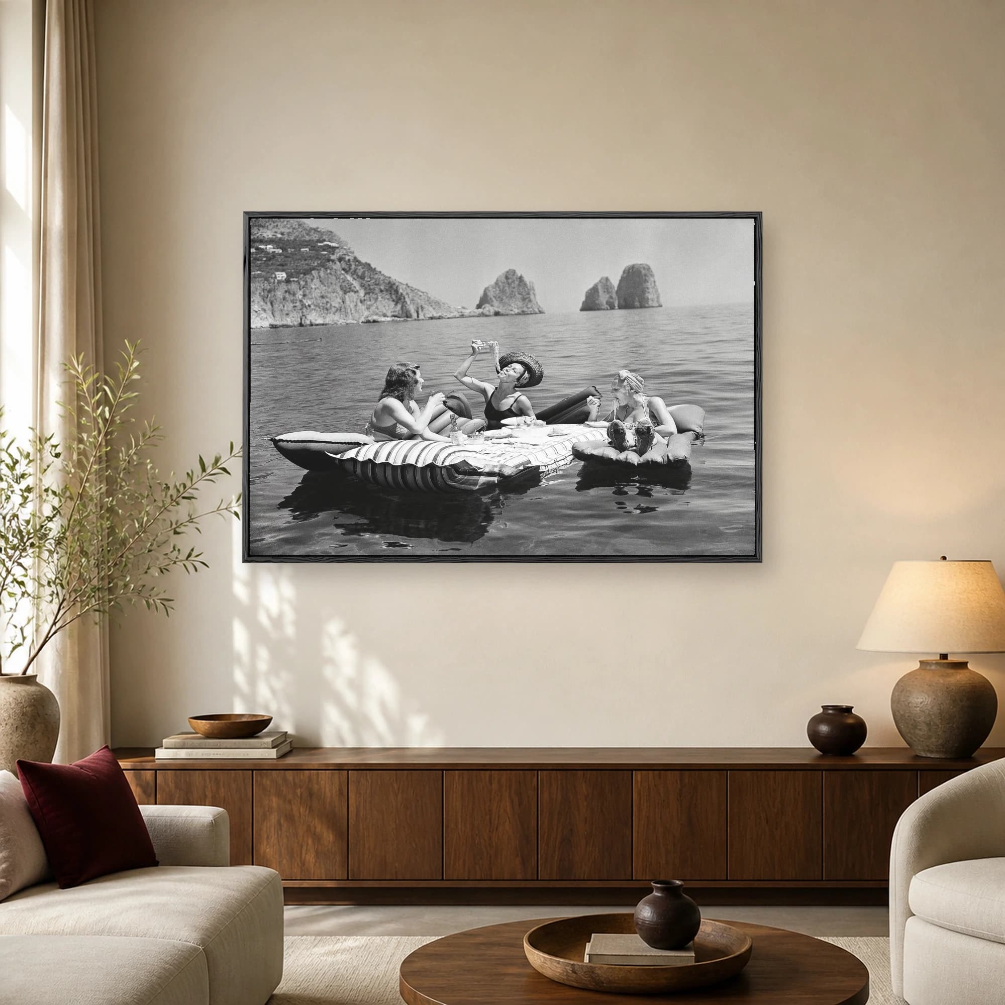 Vintage black and white photograph of three stylish women eating spaghetti on inflatable rafts floating in the sea near the Faraglioni rocks in Capri.