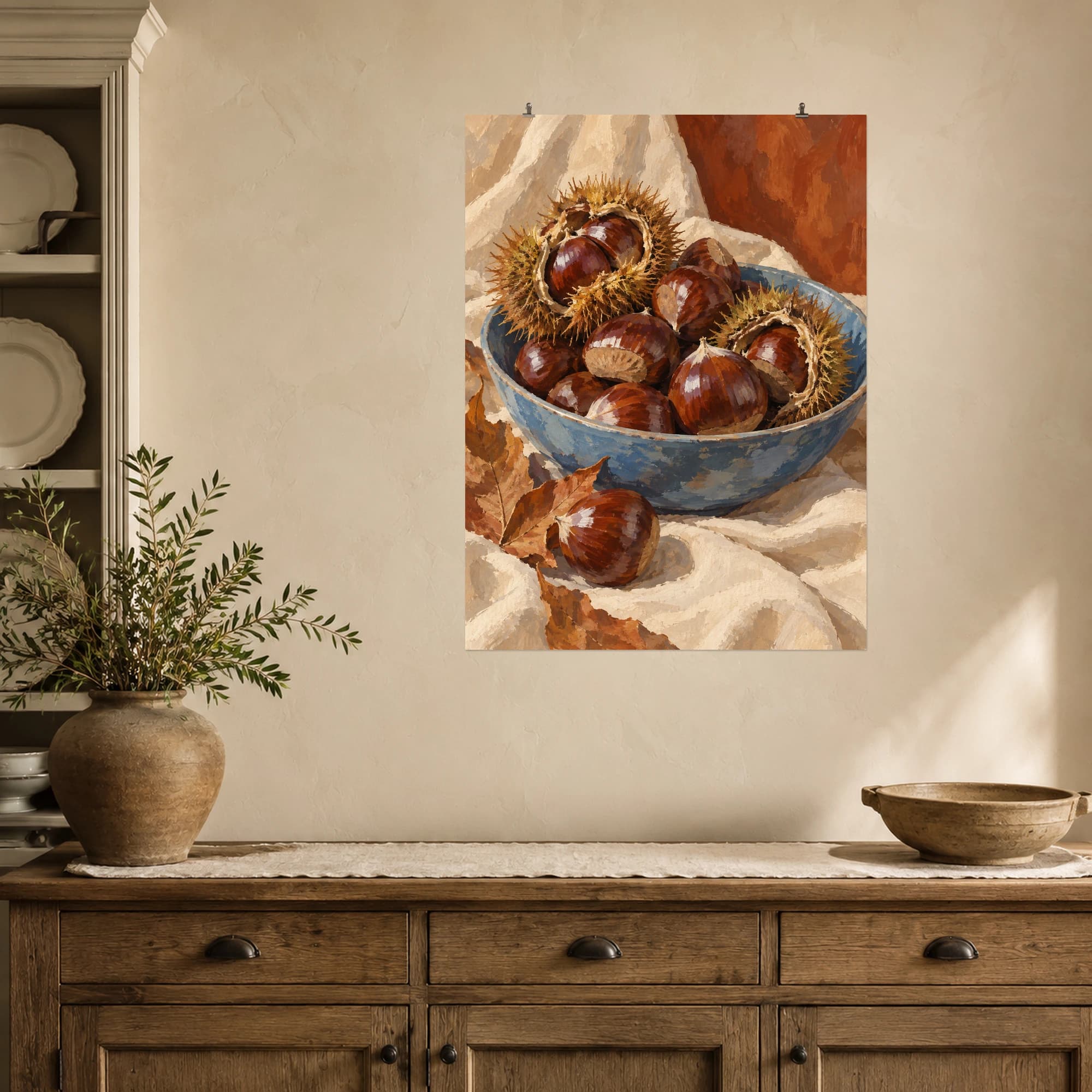 Glossy chestnuts and open spiny husks fill a weathered blue bowl. Cream linen, rust tones and scattered leaves bring a warm autumn mood to this harvest still life.