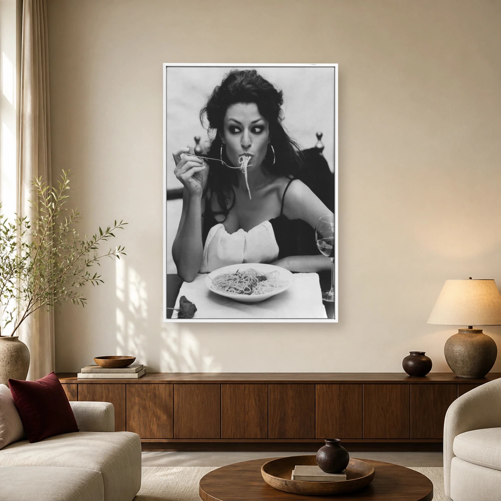 Black and white portrait of actress Sophia Loren wearing hoop earrings and eating spaghetti with a fork at a dinner table.