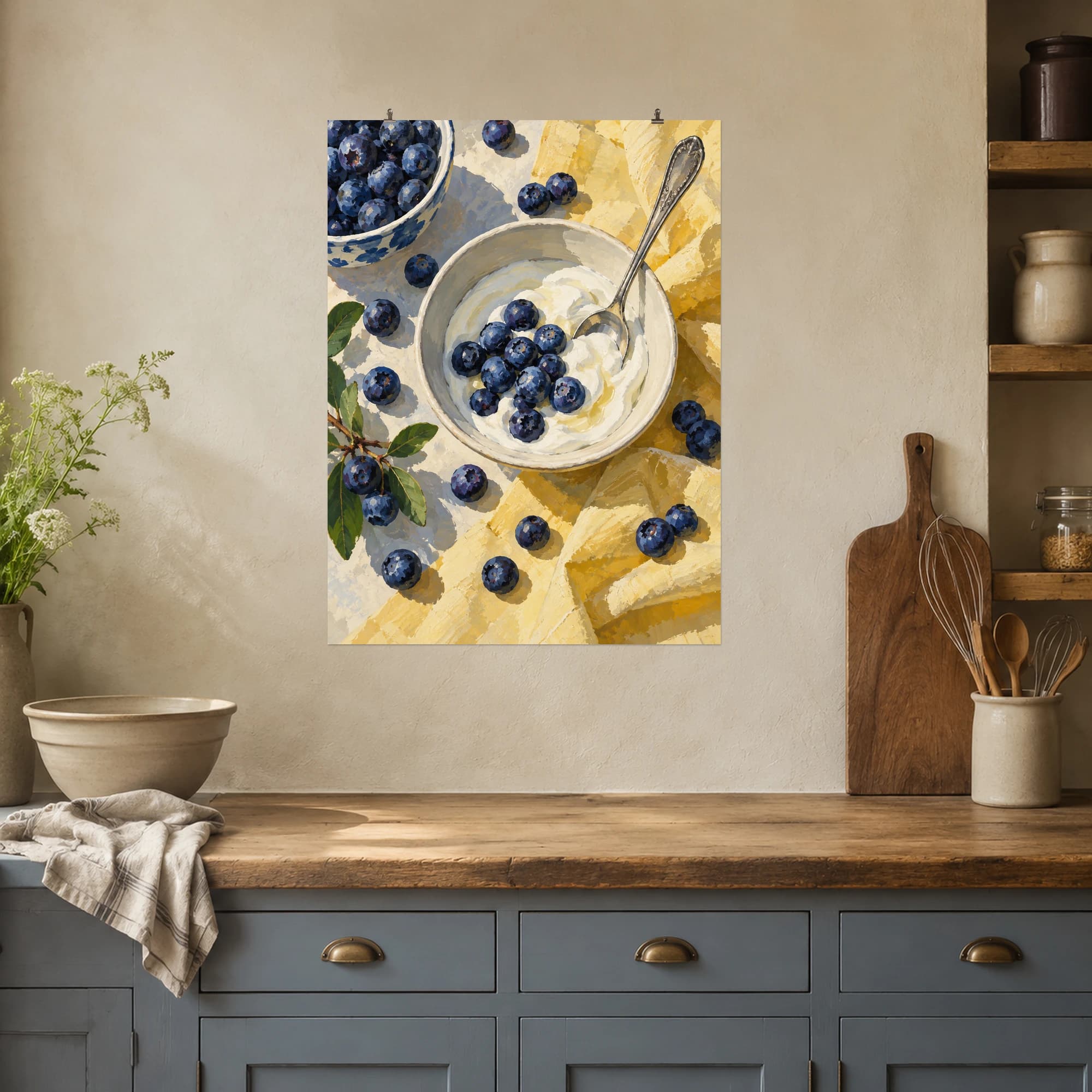 Blueberries surround a cream bowl of yogurt and a silver spoon. Pale yellow linen and deep blue fruit create a fresh, inviting breakfast composition.
