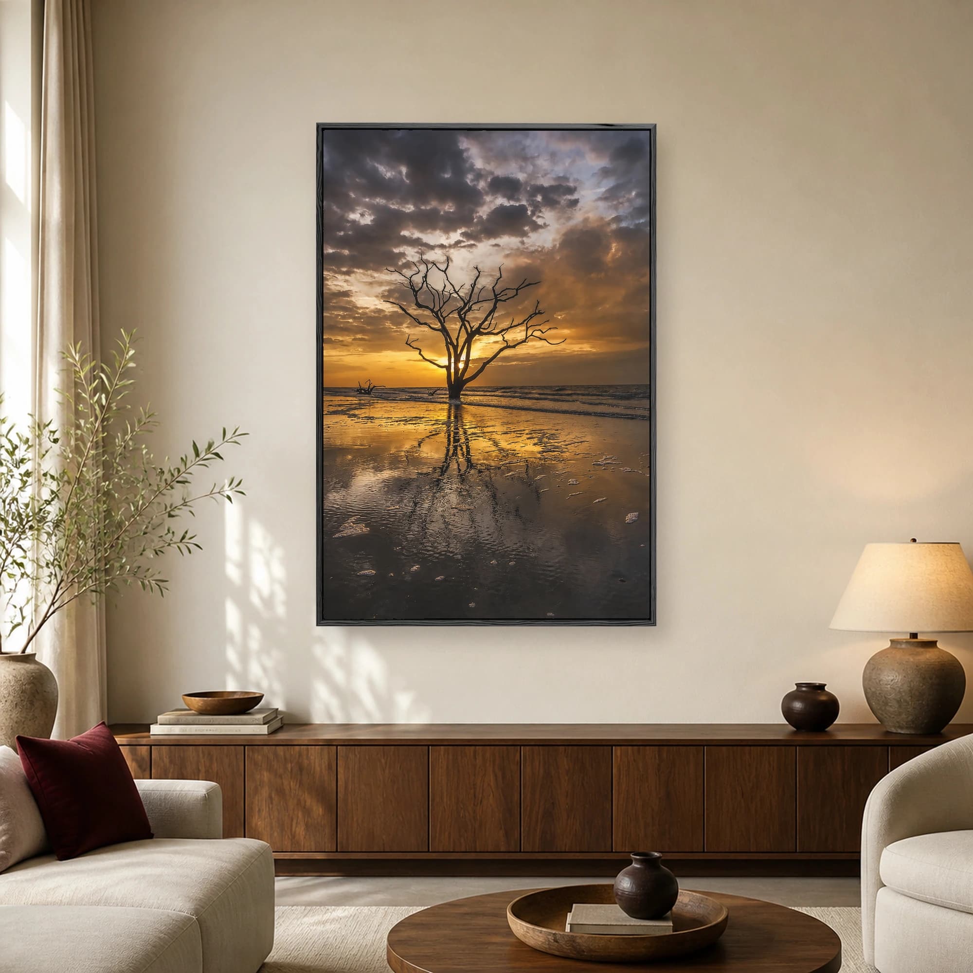 Fine art photograph of a lone skeletal tree silhouette standing in shallow water during a golden sunset, reflecting on wet sand.