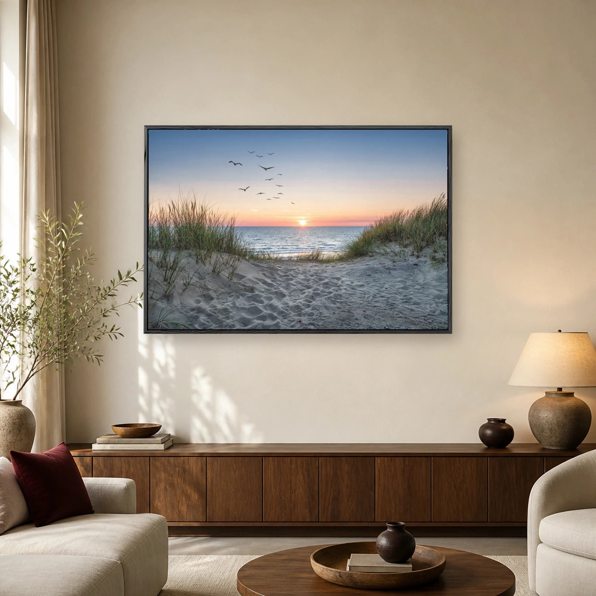 A scenic coastal photograph of a sandy path through dune grass leading to an ocean sunset with a flock of birds in the sky.