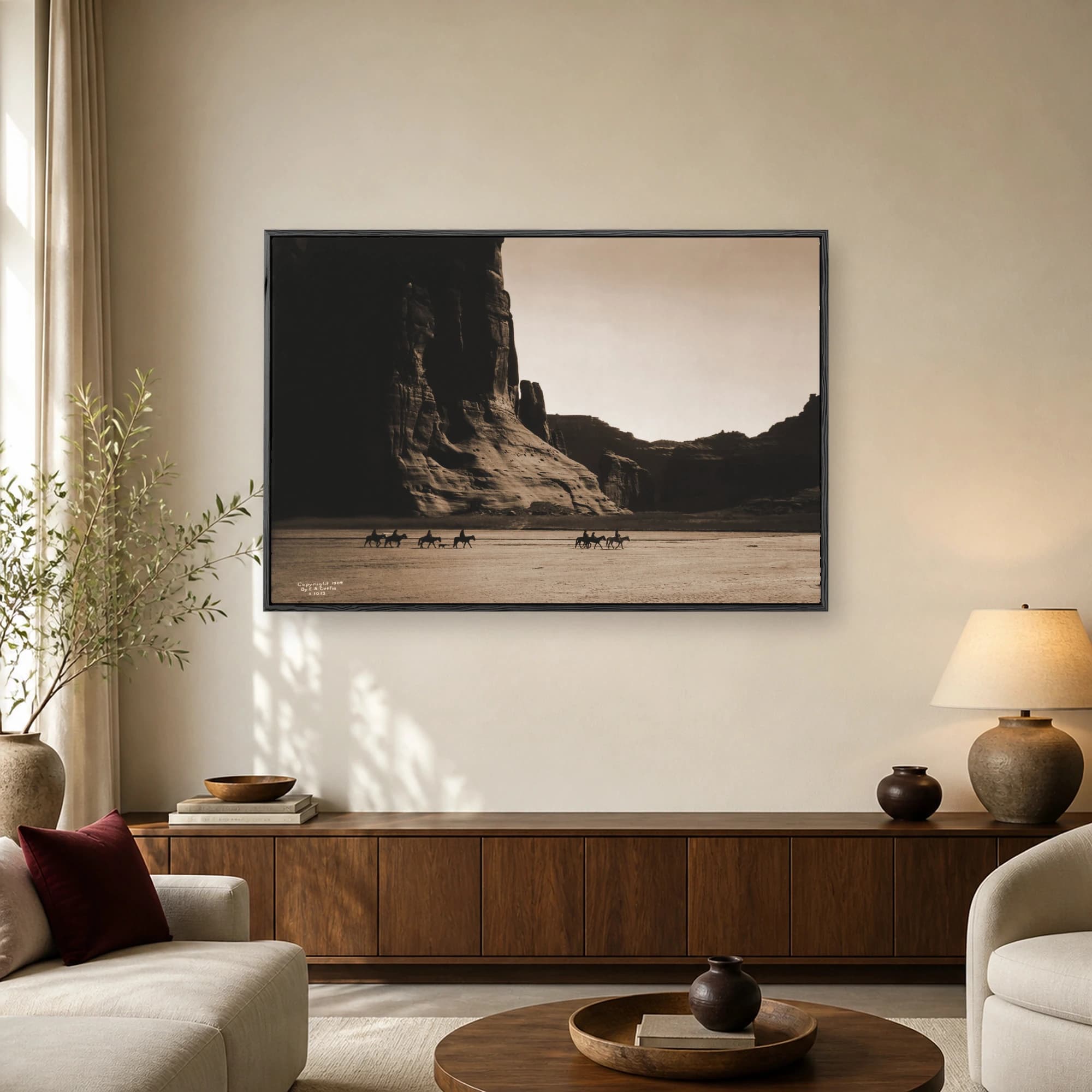 Historic sepia photograph by Edward S. Curtis from 1904 showing horsemen riding past towering canyon cliffs.