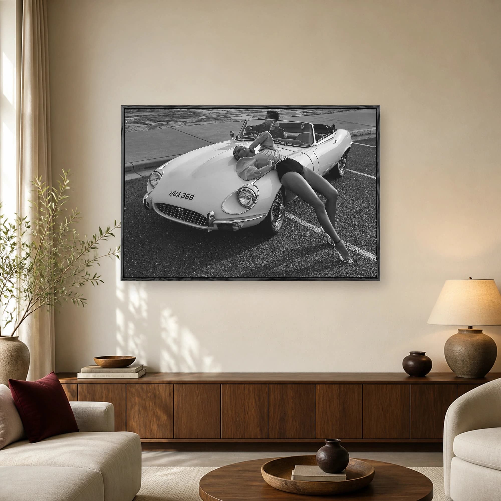 Black and white photograph of a fashion model draped over the hood of a classic vintage white convertible sports car with wire wheels.