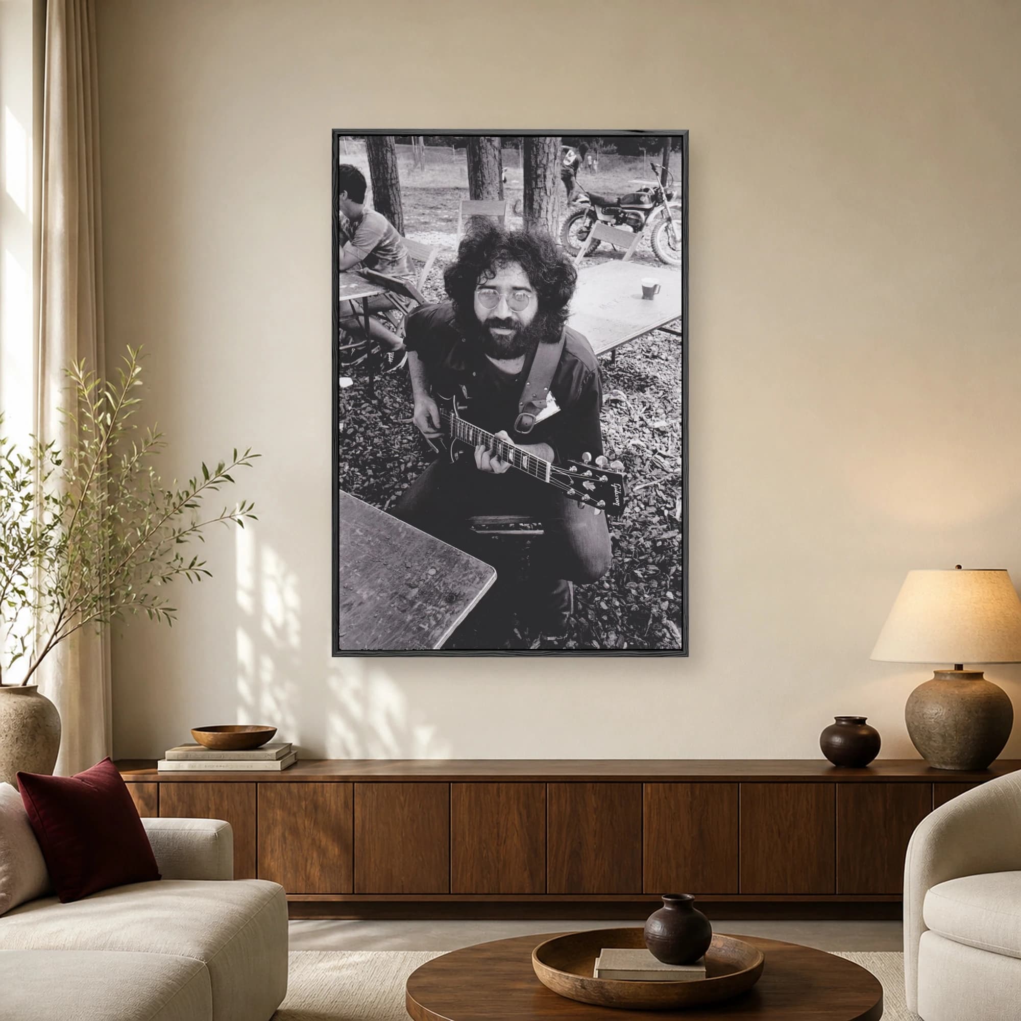 Candid black and white photograph of Jerry Garcia with beard and round glasses sitting outdoors and playing an electric guitar