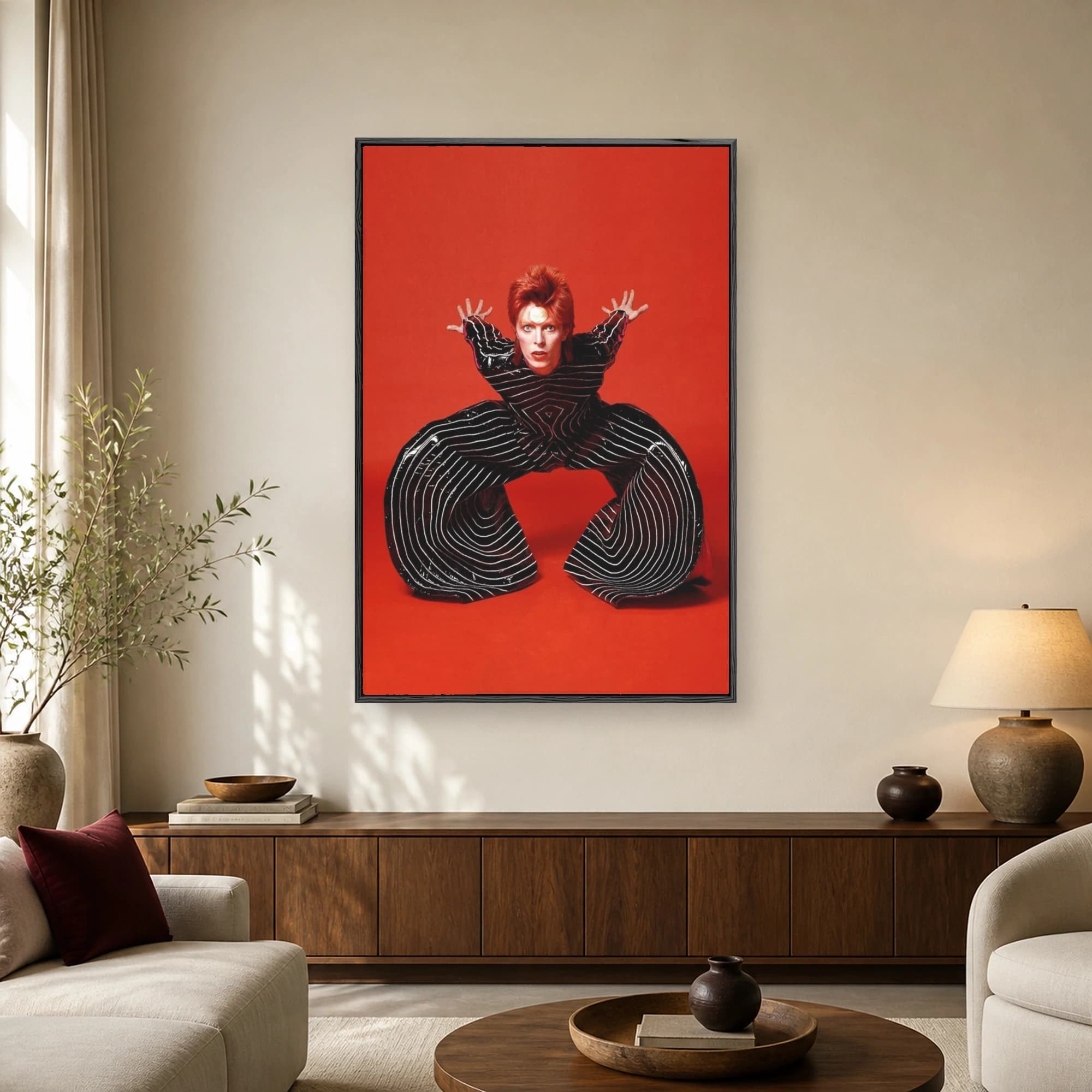 Portrait of David Bowie with red hair and gold forehead dot wearing a black and white striped wide-legged jumpsuit against a red background
