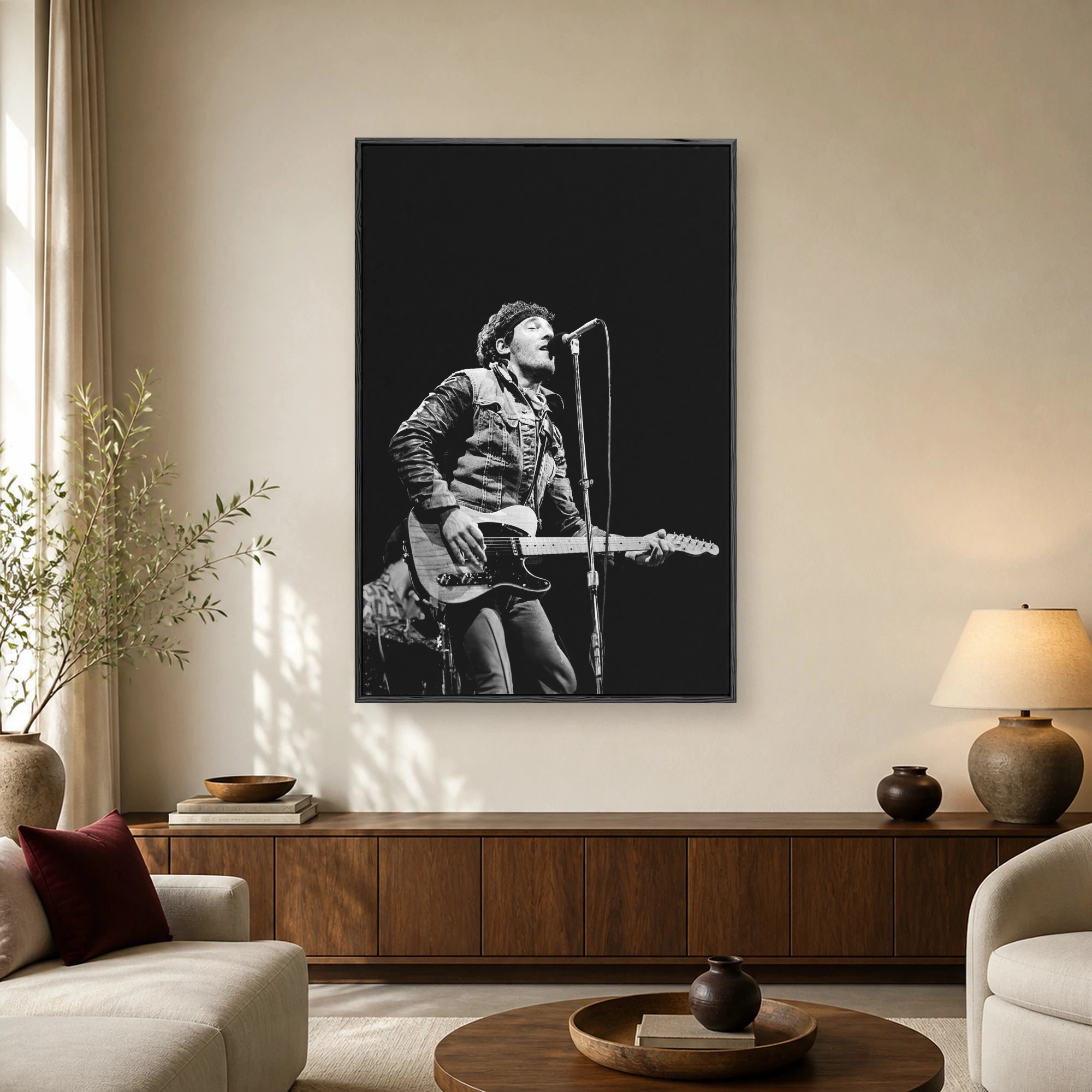 Black and white concert photograph of Bruce Springsteen singing into a microphone while playing an electric guitar against a dark background.