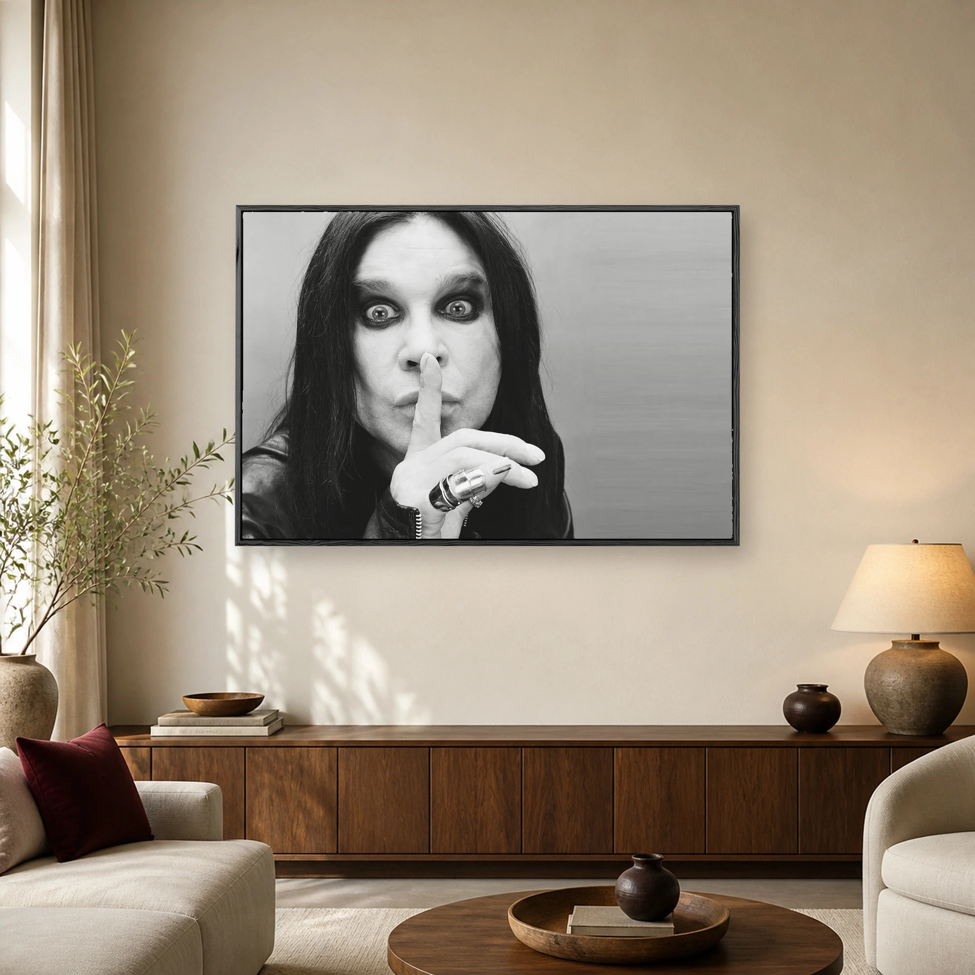 Black and white photographic portrait of rock musician Ozzy Osbourne making a hush gesture with his finger against his lips while wearing a leather jacket and dark makeup