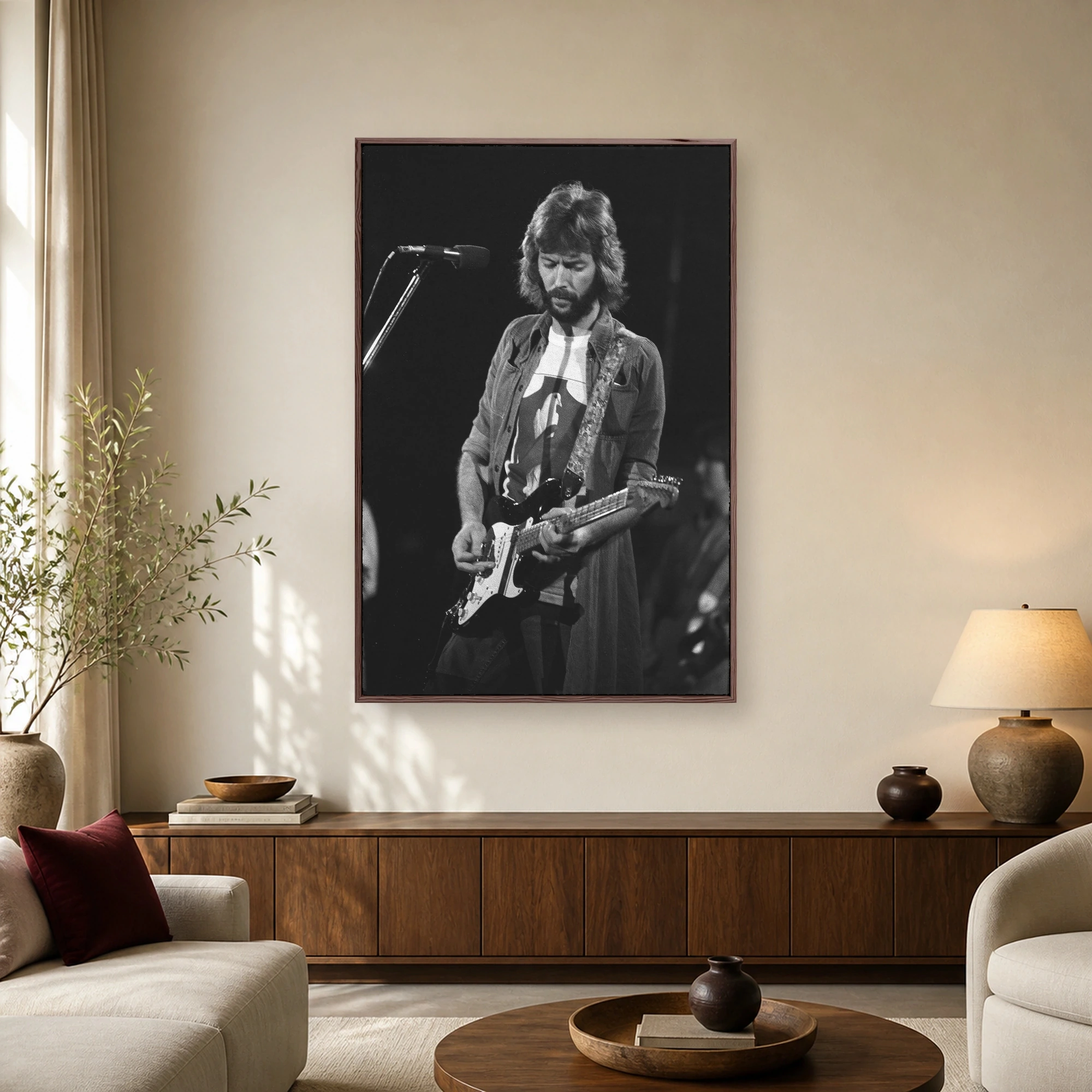 Black and white portrait of Eric Clapton with beard and 70s hair playing a Fender Stratocaster guitar on stage.
