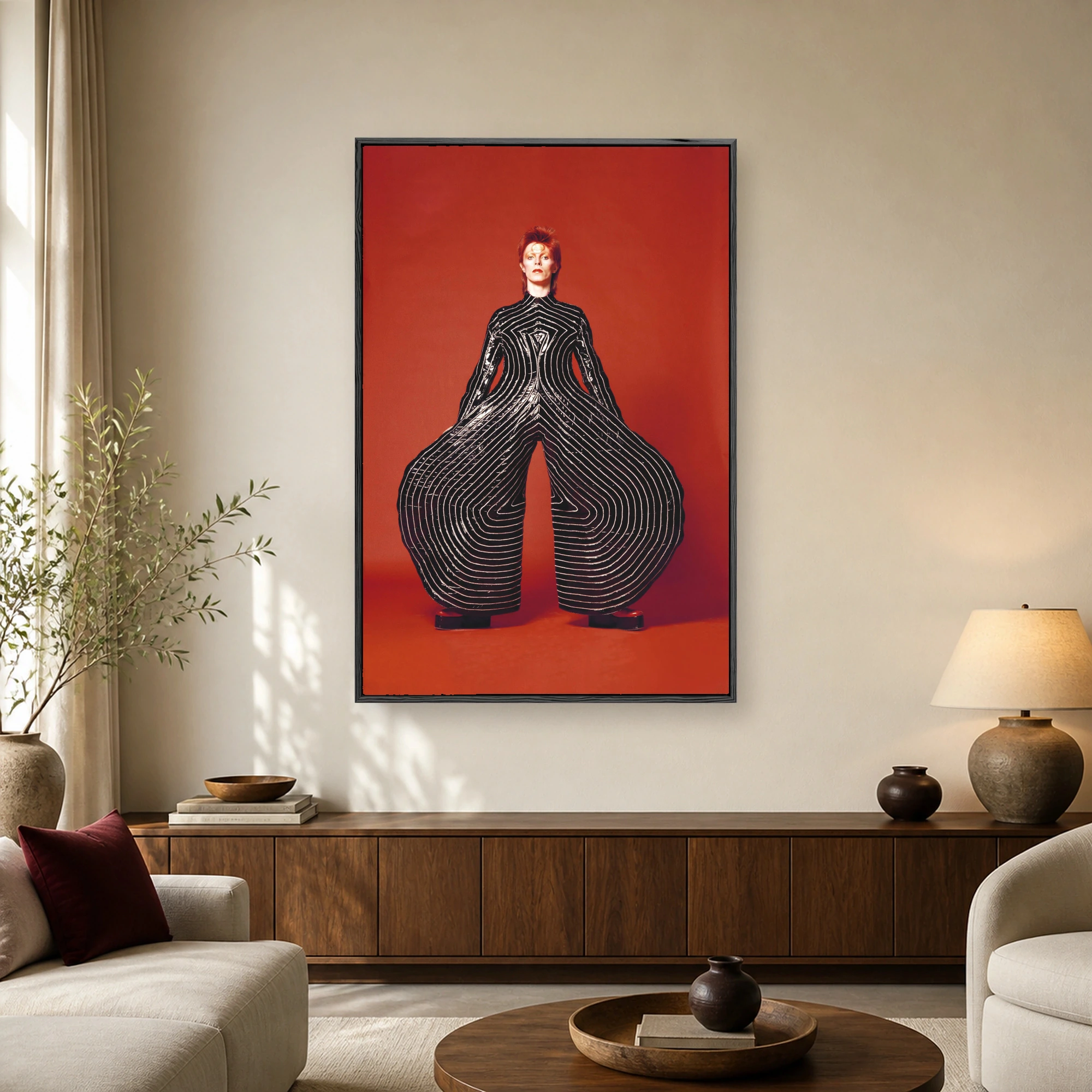Full-length studio portrait of David Bowie wearing a black vinyl jumpsuit with wide circular leg flares on a bright red background.