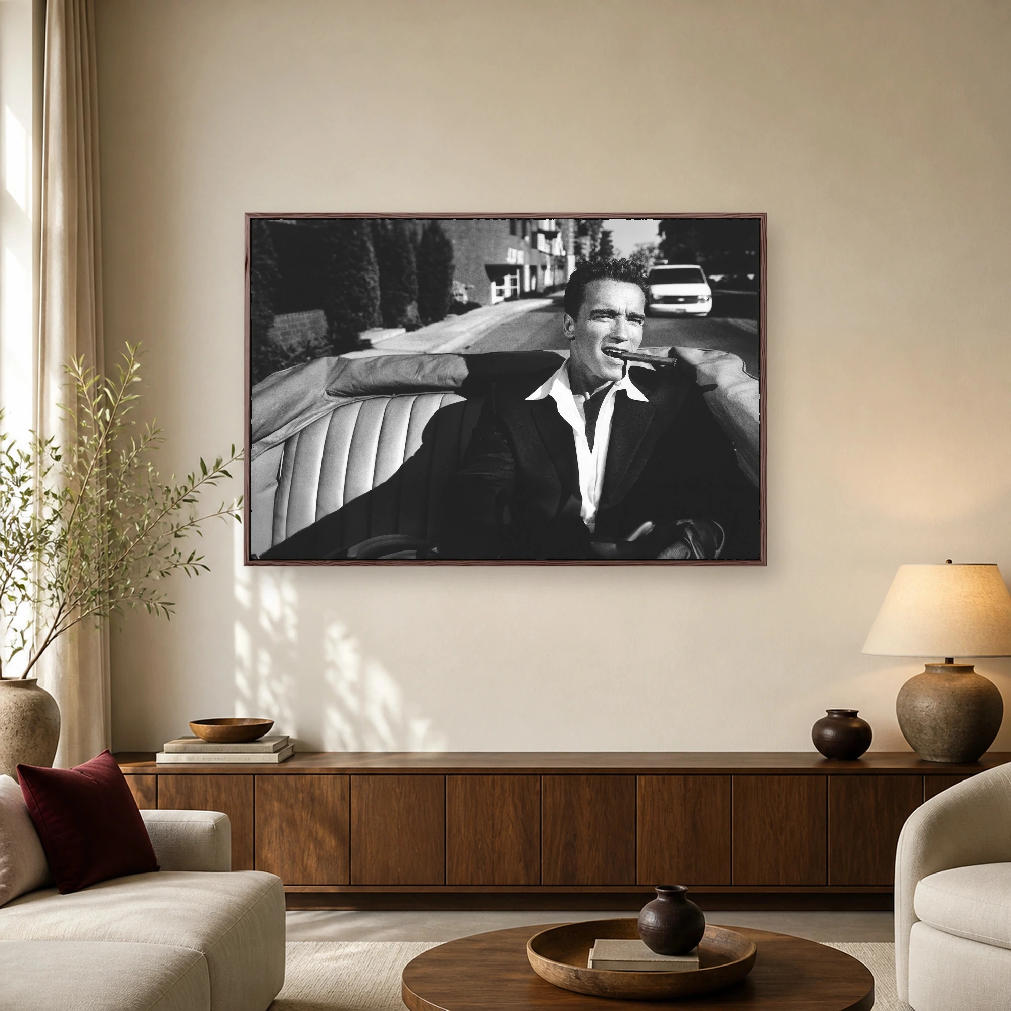 Black and white portrait of Arnold Schwarzenegger in a convertible car with a cigar in his mouth, wearing a suit and open white shirt.