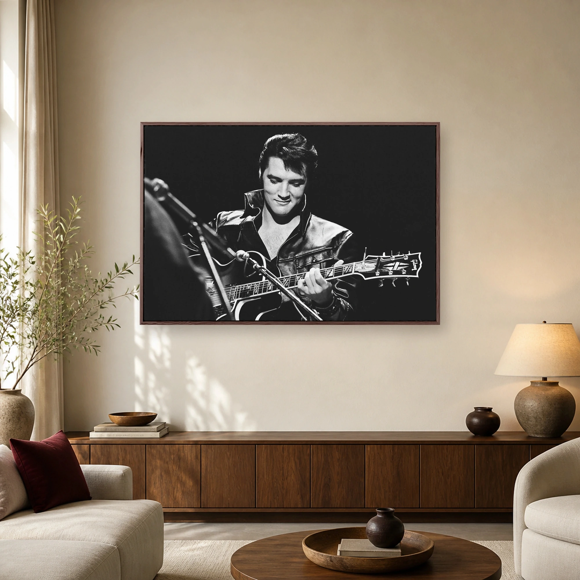 Black and white portrait photograph of Elvis Presley playing a Gibson guitar on stage wearing a black leather jacket with high collar.